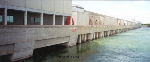 The long concrete powerhouse of the Moses-Saunders Power Dam on the St. Lawrence River, with river water flowing along its base.