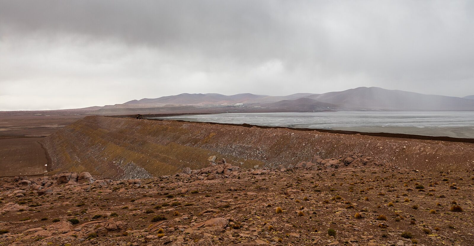 A wide open pit copper mine cut into a dry, brown Andean plateau under a pale sky.