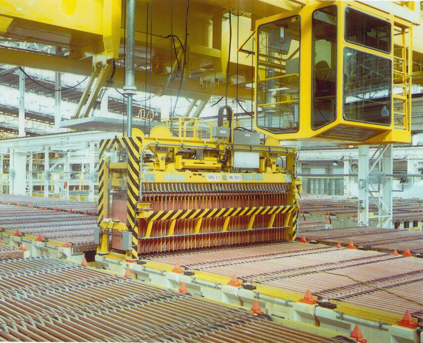 Rows of copper cathode plates in a refinery tankhouse, with a yellow overhead crane lifting a rack of cathodes.
